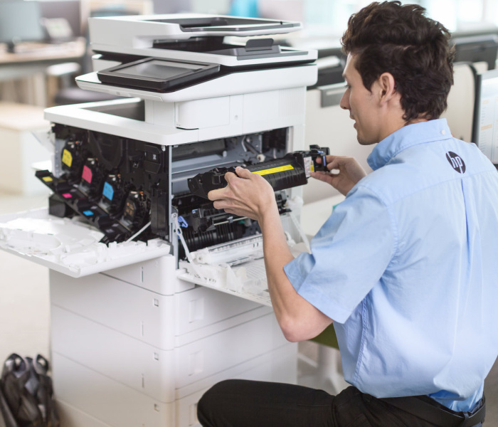 A printer technician with a manual open on a HP Elite x2 1012 G1 while replacing a part for a HP Color LaserJet Enterprise Flow MFP M577z.